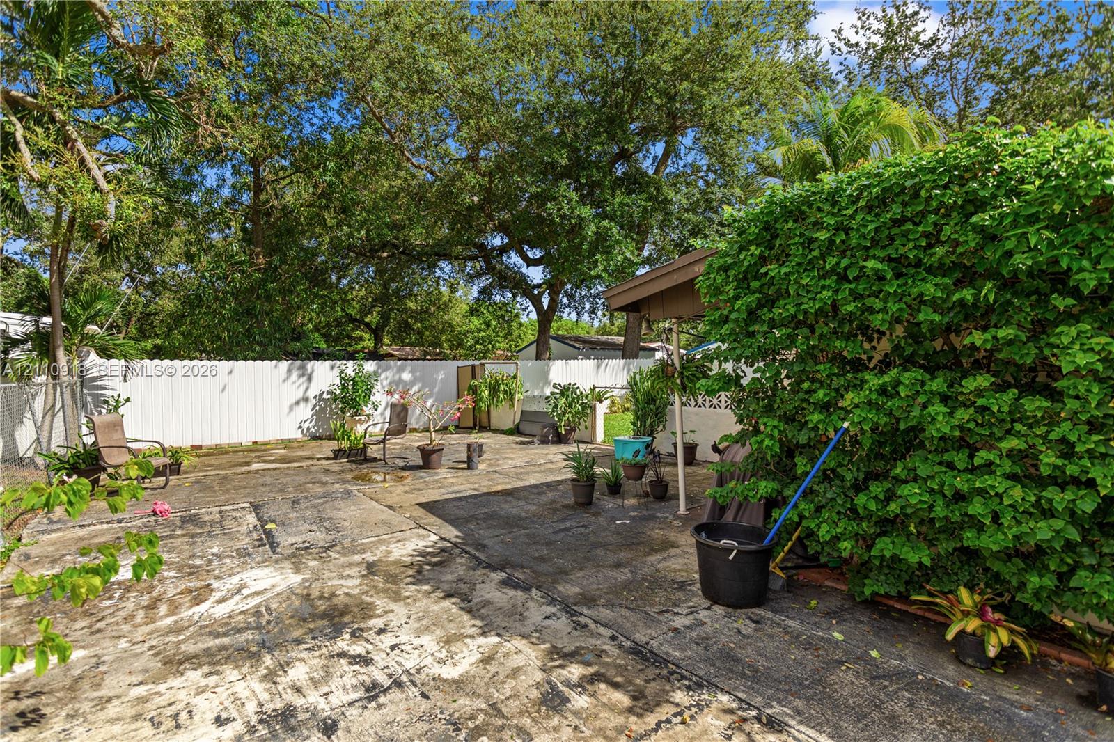 Fenced backyard featuring a concrete patio, a covered structure, and mature trees Fenced backyard featuring a concrete patio, a covered structure, and mature trees