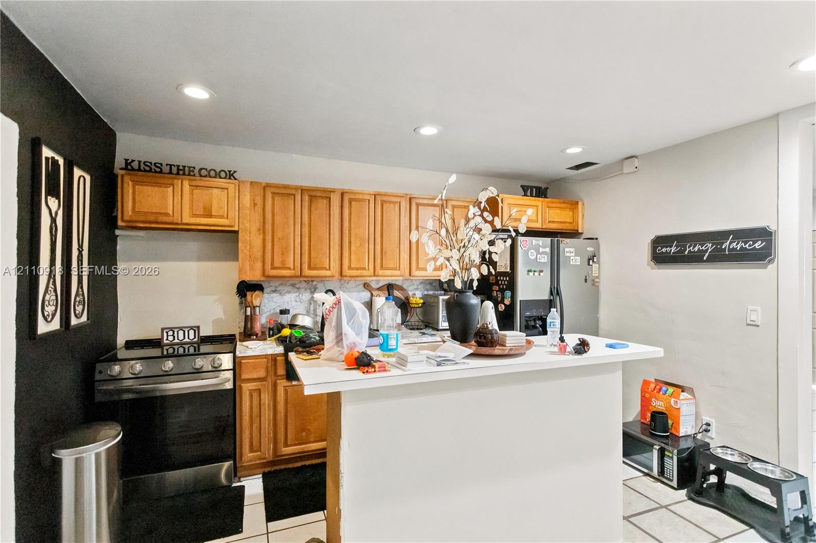 Kitchen featuring light-finish cabinetry, a breakfast bar with a solid-surface countertop, recessed ceiling lighting, and tile flooring