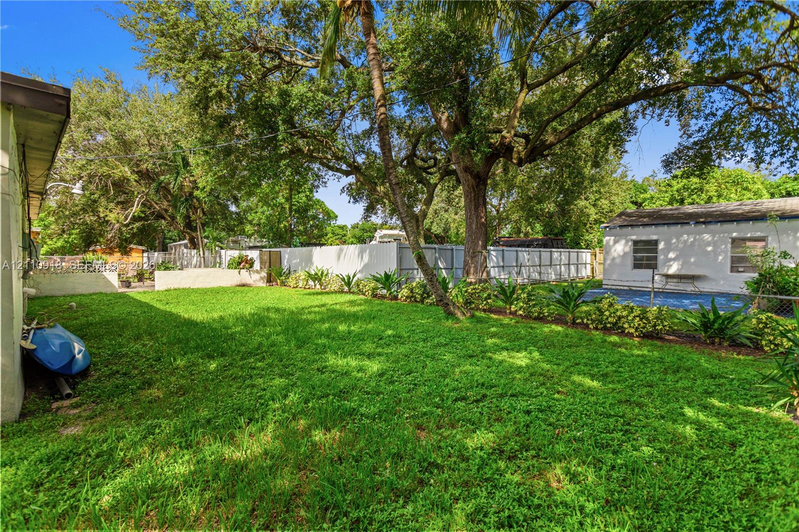 Expansive backyard featuring a manicured lawn, mature trees, privacy fencing, and a swimming pool