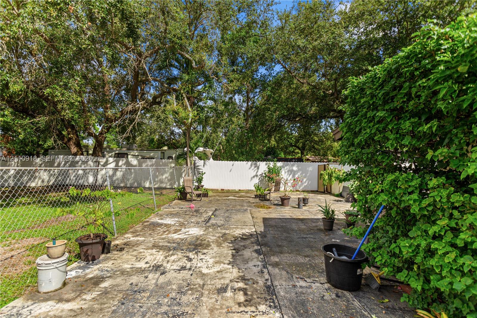 Backyard featuring a concrete patio, perimeter chain-link and privacy fencing, and mature canopy trees Backyard featuring a concrete patio, perimeter chain-link and privacy fencing, and mature canopy trees