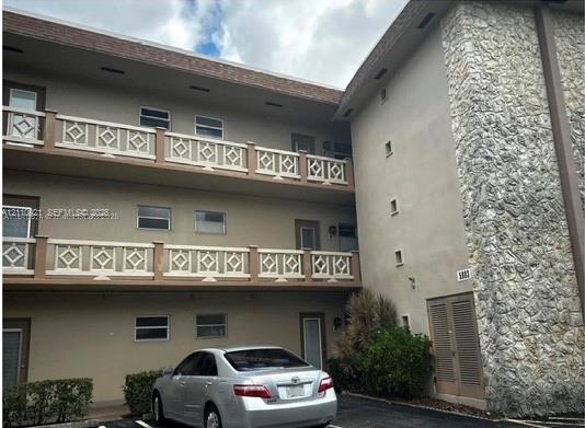 Three-story building exterior featuring textured stone masonry facade, multi-level balconies with geometric lattice railings, and exterior-access entry doors