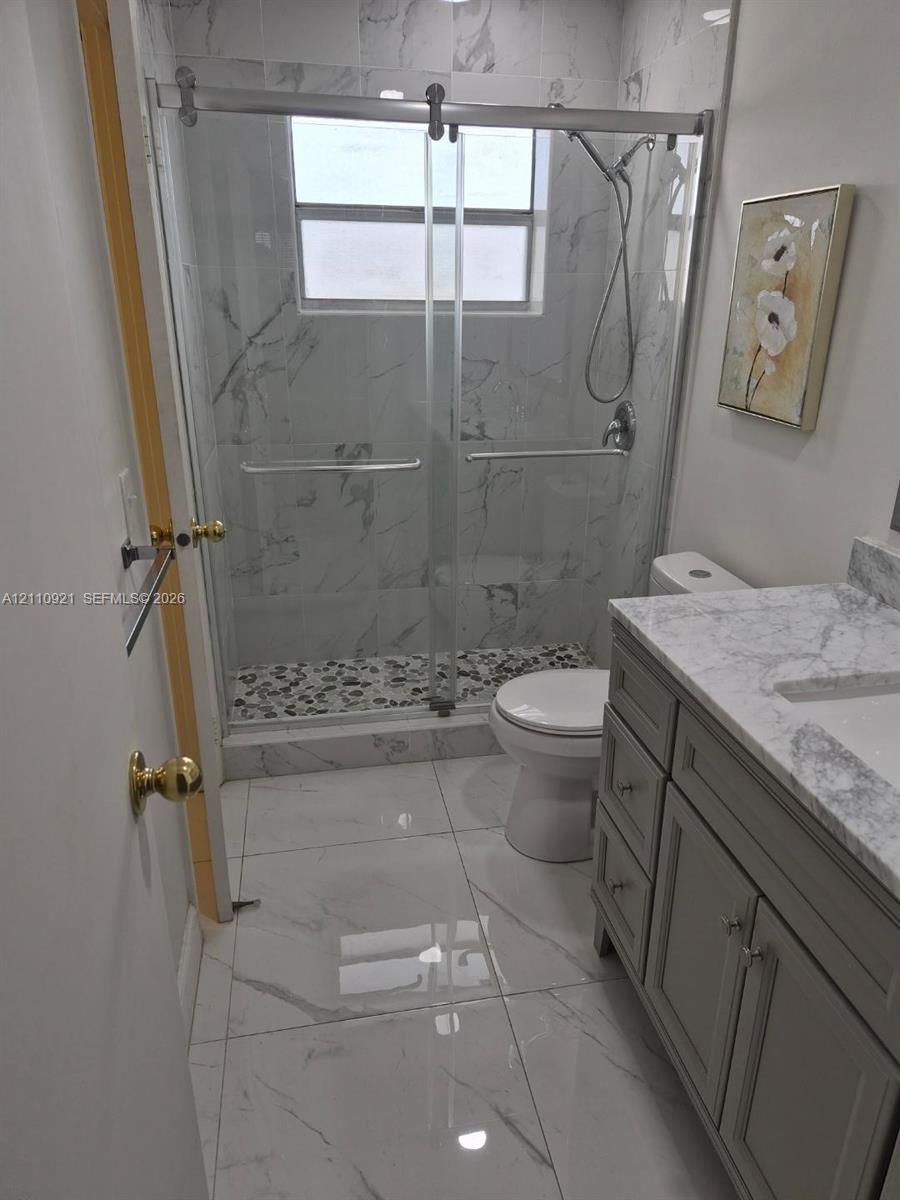 Walk-in shower with a sliding glass door, stone-patterned tile wall surround, and pebble-style shower floor