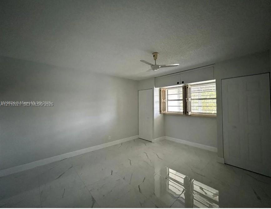 Large-format white tile flooring with grey veining, neutral-toned walls, a ceiling-mounted fan, and two built-in closets