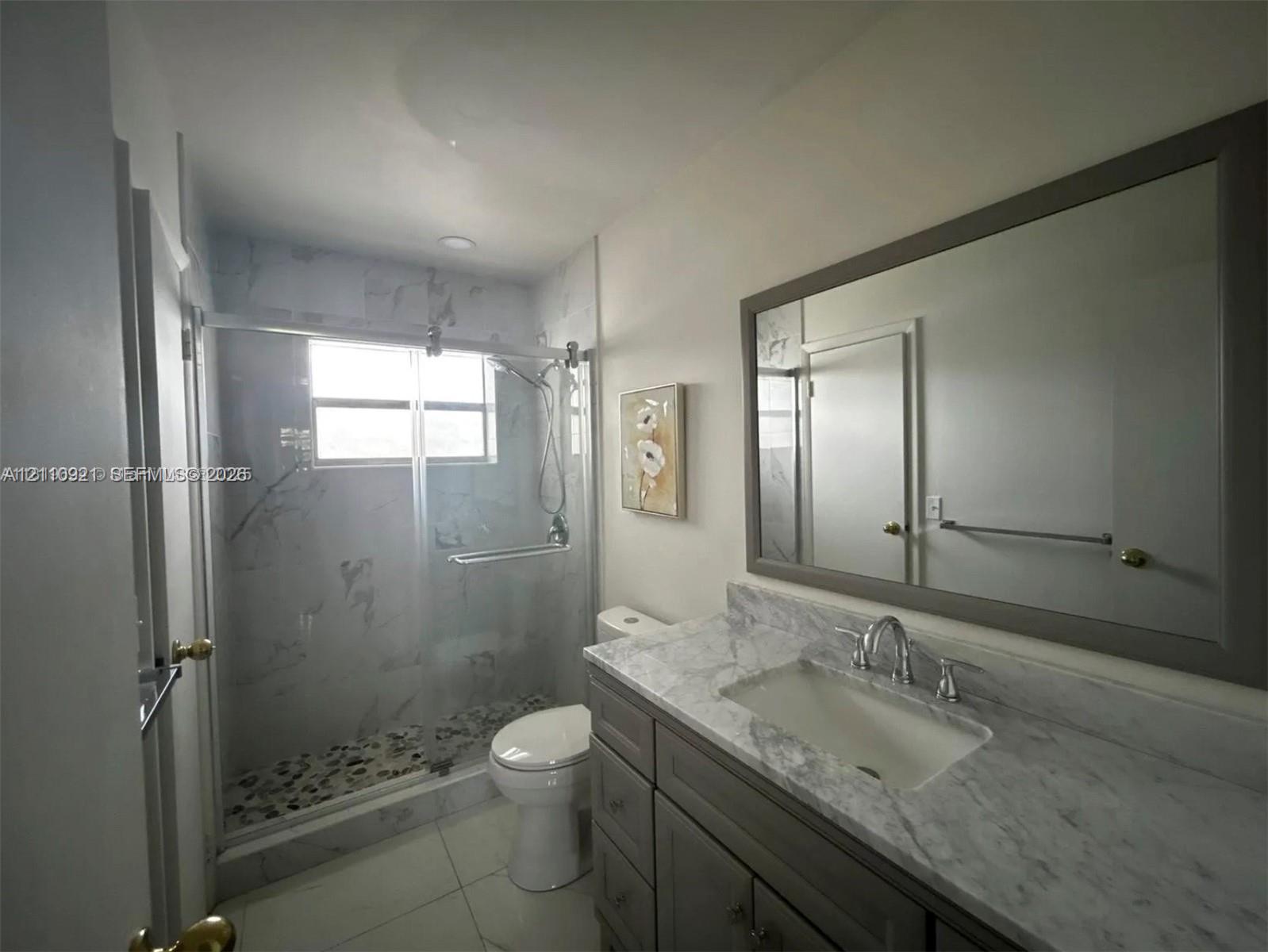 Bathroom featuring a stone-surface vanity with an integrated basin, a large framed wall mirror, a glass-enclosed shower with tiled walls, and stone-tile flooring