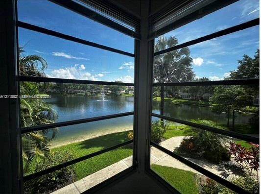 Corner window with horizontal louvers, overlooking a lake with a fountain, manicured lawn, paved walkway, and mature landscaping