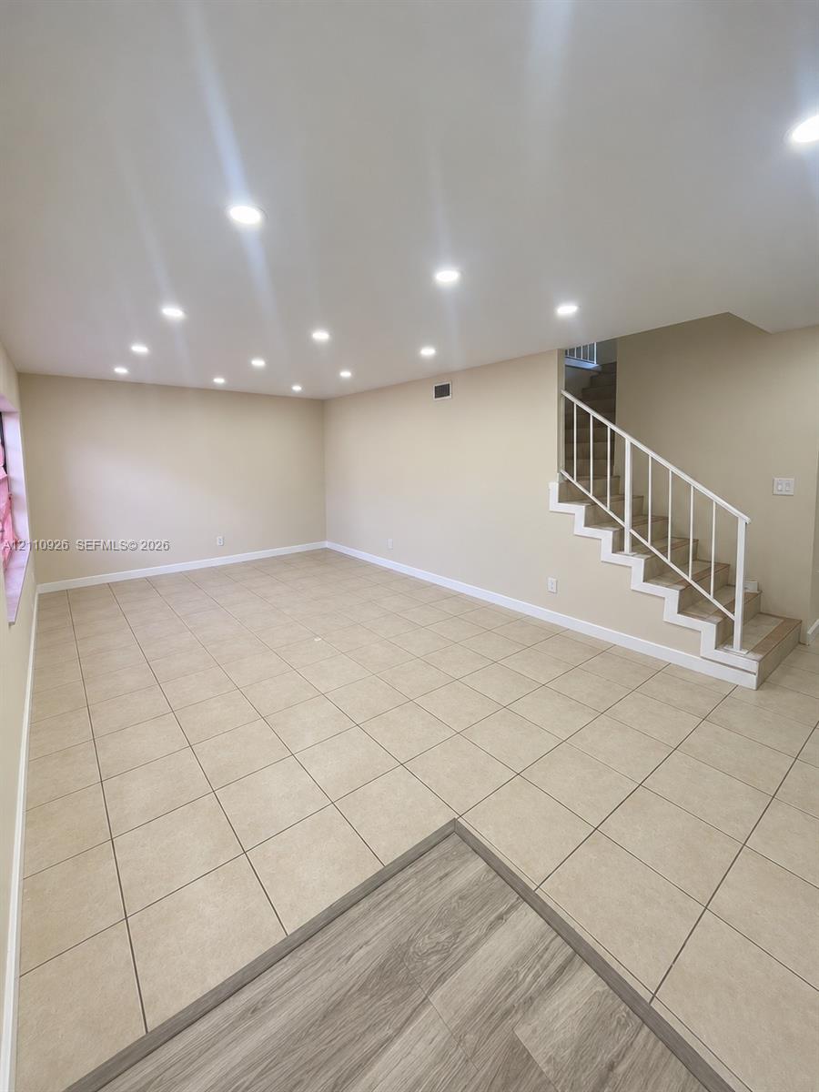 Open interior space featuring neutral tile flooring, recessed ceiling lighting, and a staircase with a white metal railing