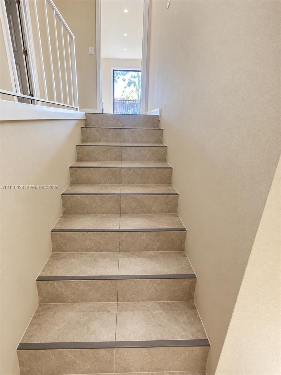 Staircase featuring neutral-toned ceramic tiling, integrated stair nosing, and a metal railing