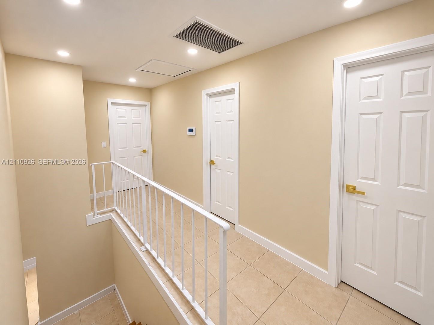 Hallway featuring neutral-toned walls, tile flooring, white six-panel doors with gold-tone hardware, and a white metal safety railing