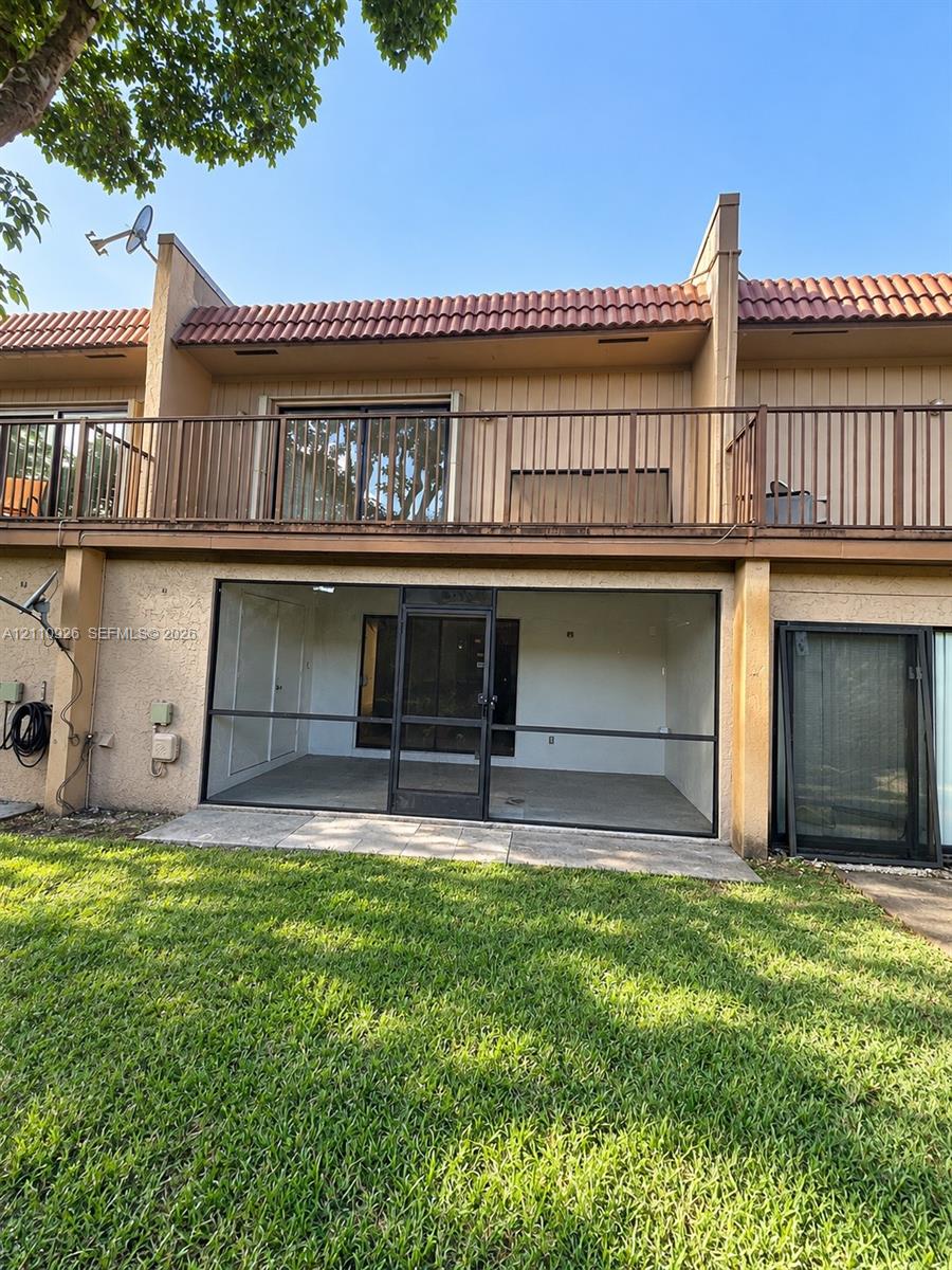 Exterior featuring a tile roof, second-story balcony with metal railings, and a ground-level enclosed screened patio