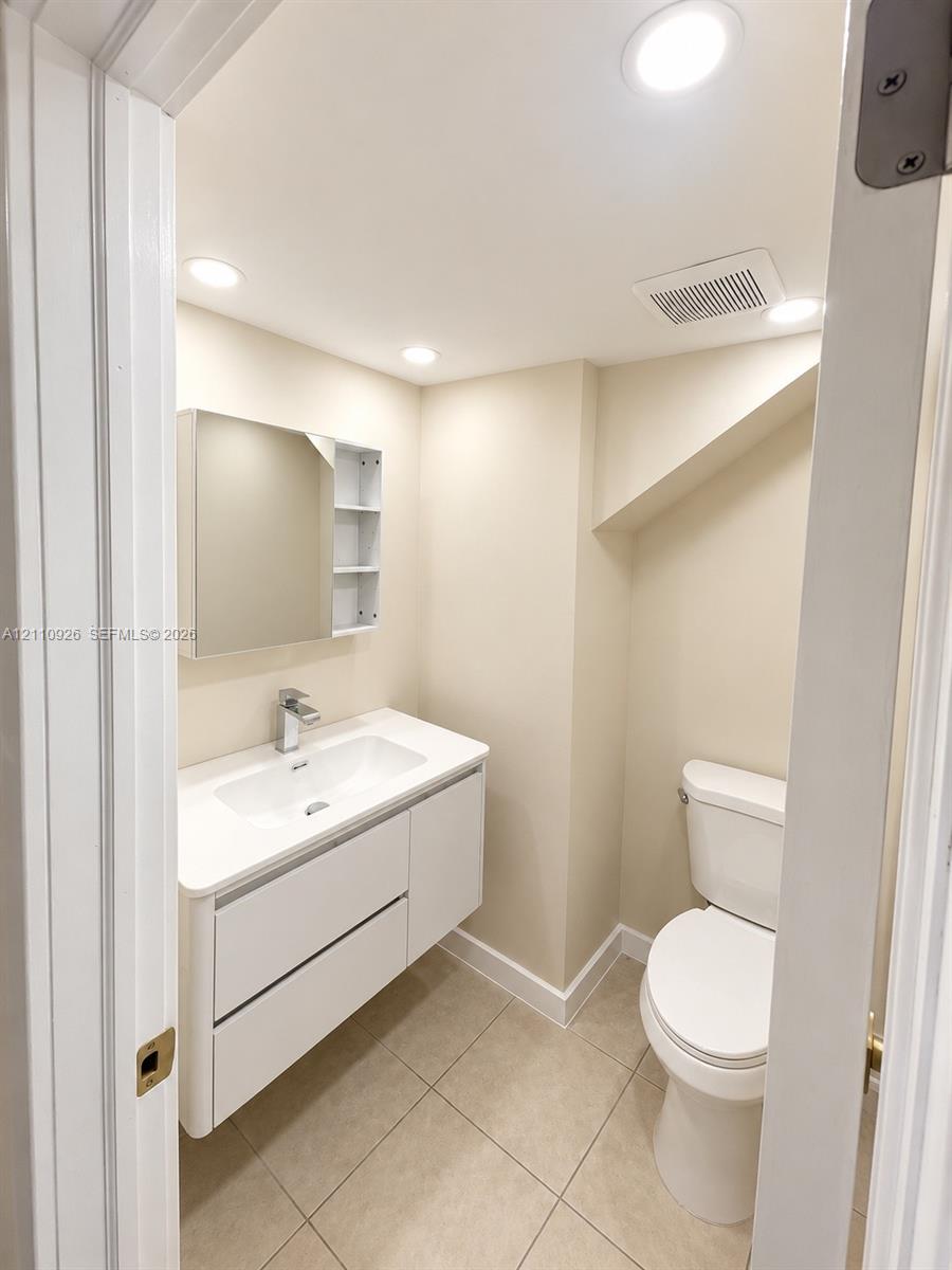 Modern floating vanity with a white countertop and integrated sink, recessed lighting, and a mirrored medicine cabinet