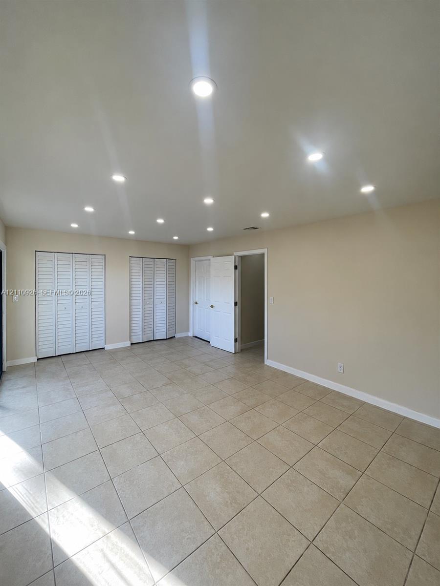 Neutral-toned interior space featuring light-colored tile flooring, multiple recessed ceiling lights, and two sets of bi-fold closet doors