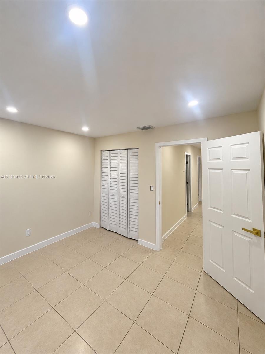 Neutral-toned interior space featuring large-format tile flooring, recessed ceiling lighting, and a bi-fold louvered closet door