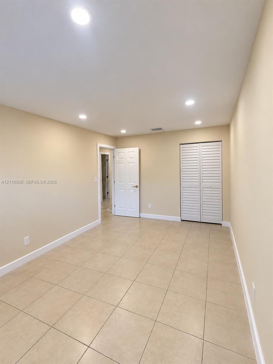 Neutral-toned tile flooring, recessed ceiling lighting, and louvered closet doors