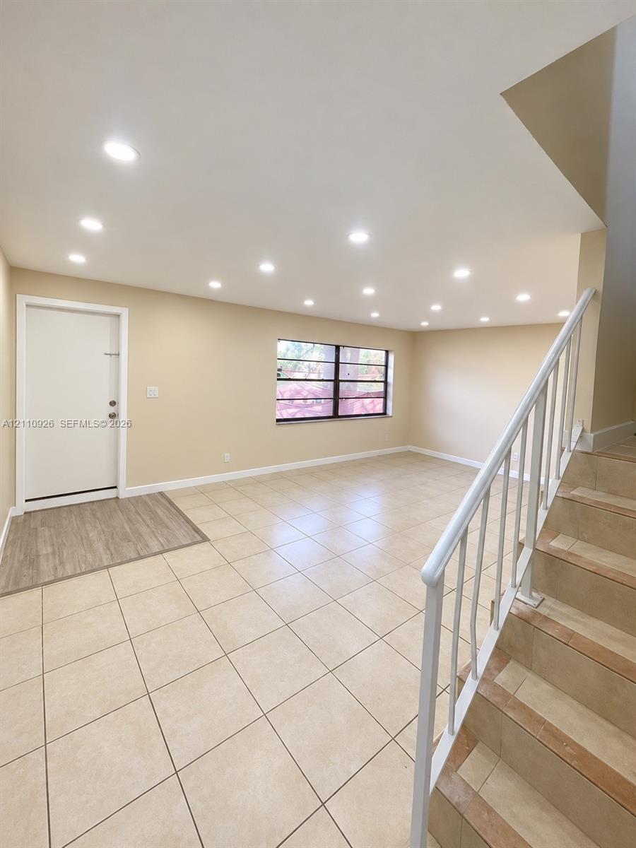 Open interior space featuring recessed ceiling lighting, large-format tile flooring, wood-finish entryway flooring, and a metal staircase railing