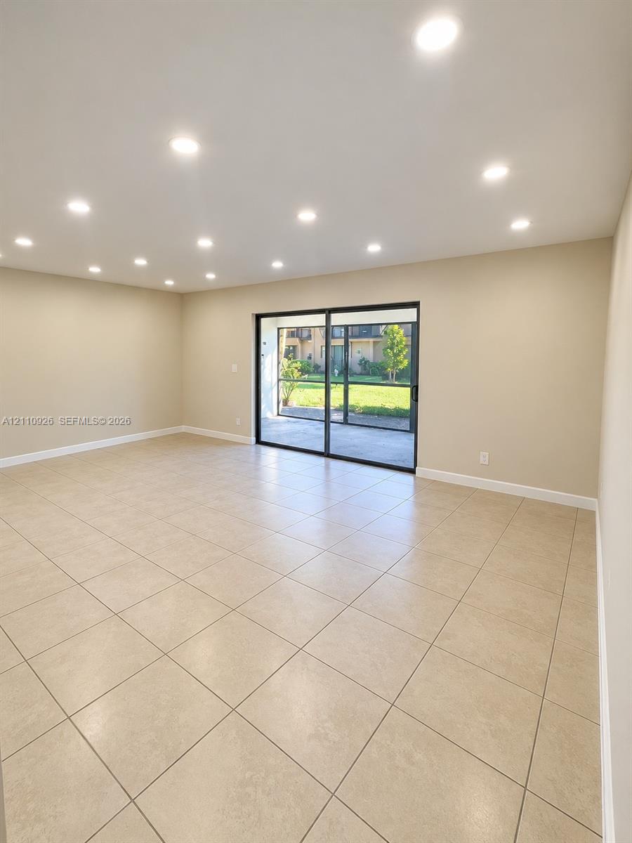 Neutral-toned room featuring large-format tile flooring, recessed ceiling lighting, and sliding glass doors with black framing