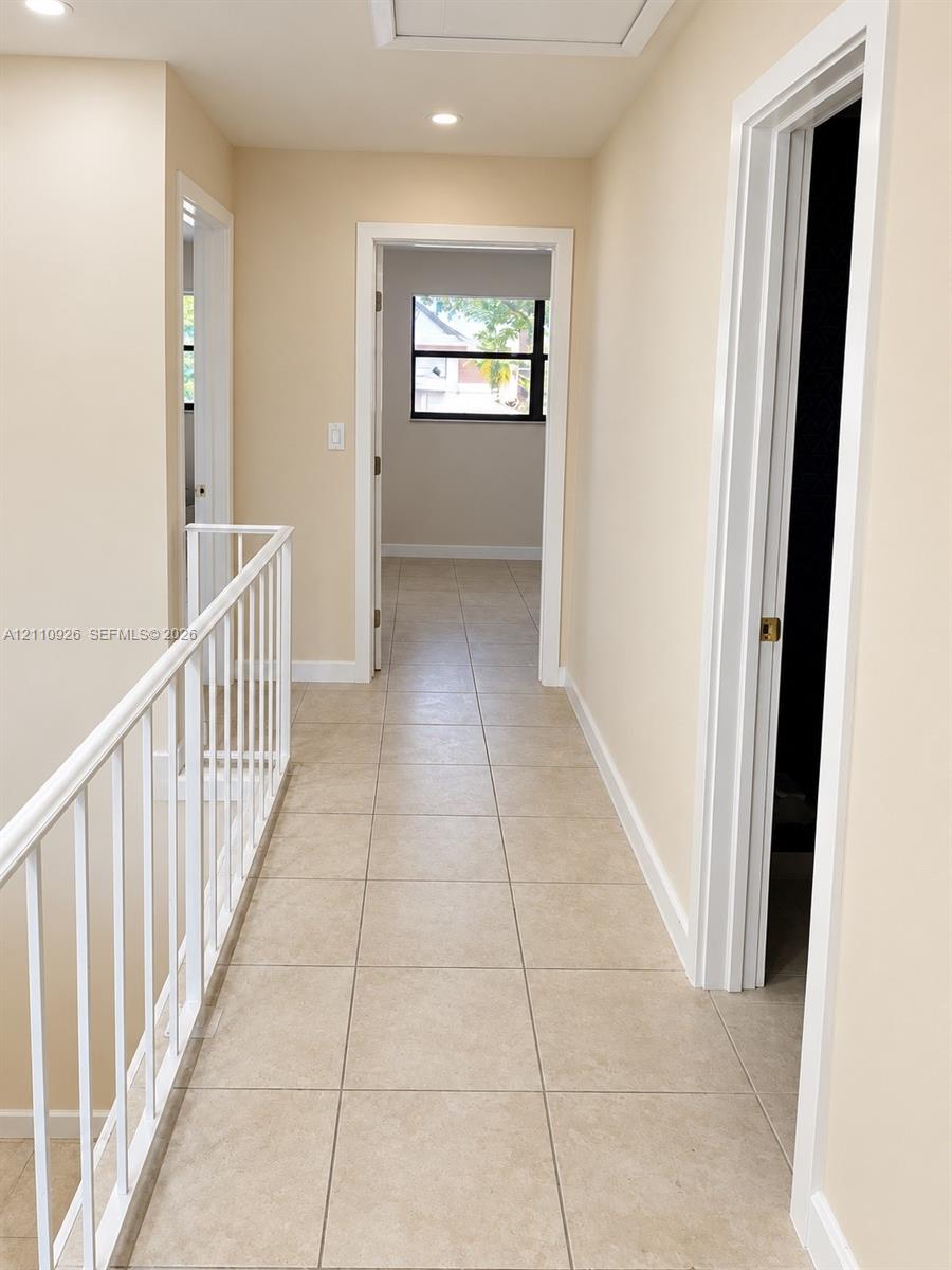 Hallway featuring tile flooring, white metal railing, recessed lighting, and multiple interior doorways