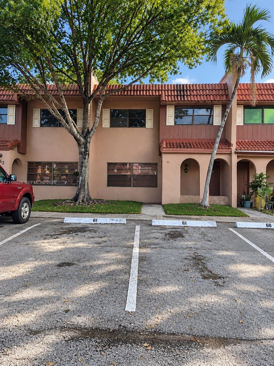 Two-story stucco exterior featuring a red tile roof, arched entryway, and dedicated assigned parking spaces