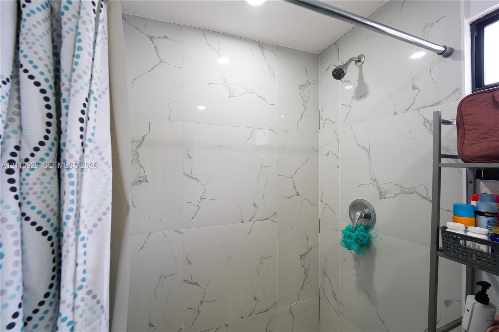 Shower stall featuring large-format white stone-finish wall tiling with grey veining, a chrome fixed shower head, and a chrome single-handle pressure balance valve