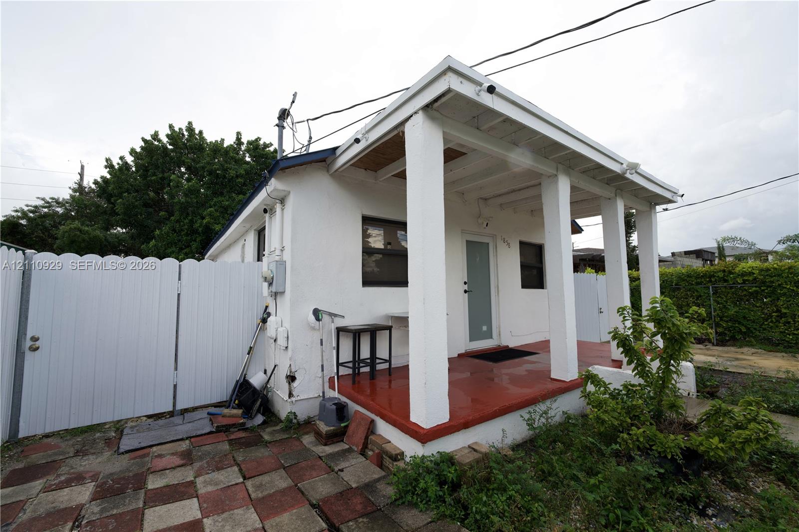 White stucco exterior featuring a covered front porch with squared columns, a paved patio area, and a white privacy gate