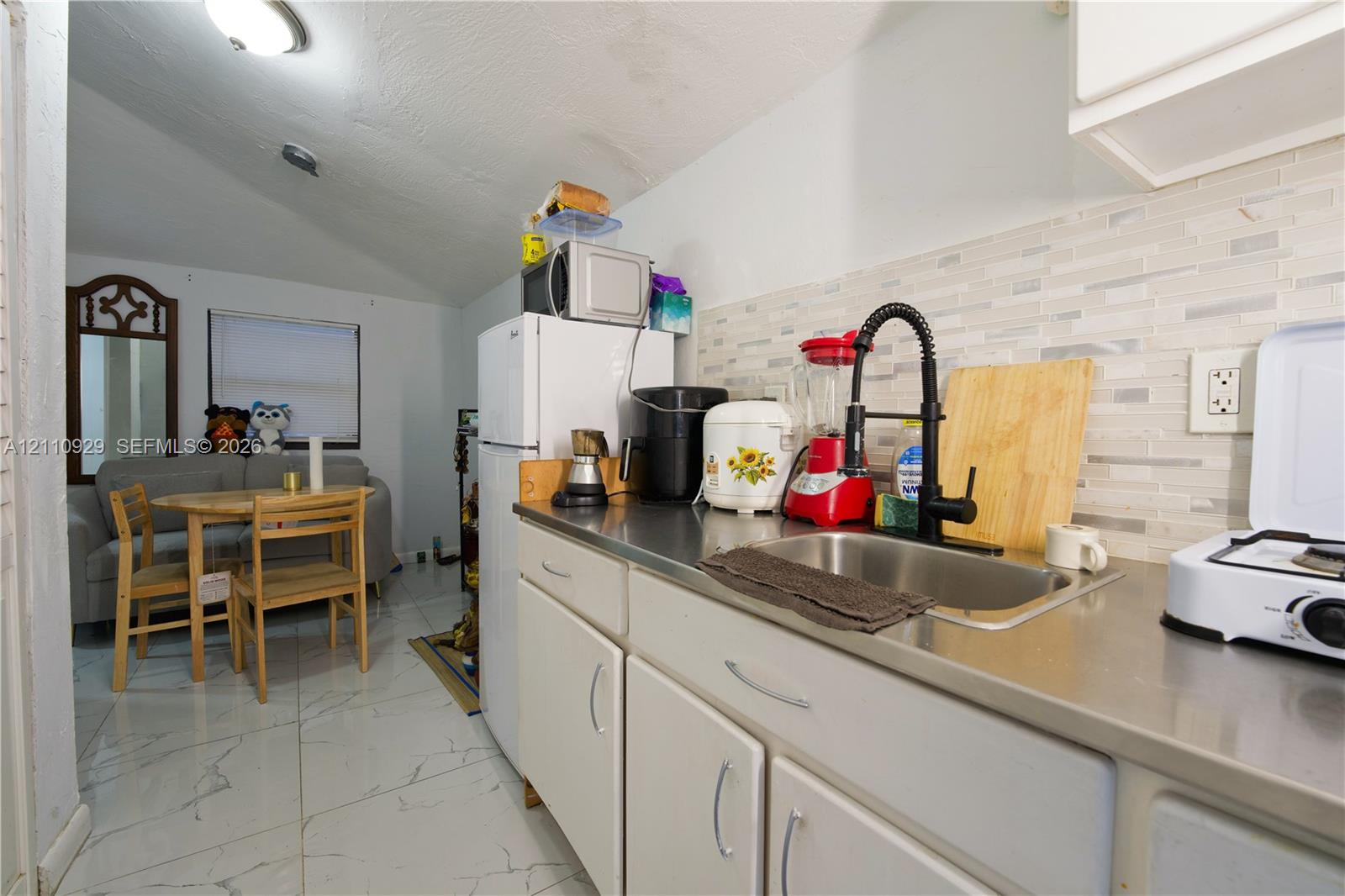 Kitchen featuring white cabinetry, metallic countertop, stainless steel sink with matte black gooseneck faucet, stone-finish tile flooring, and a textured backsplash