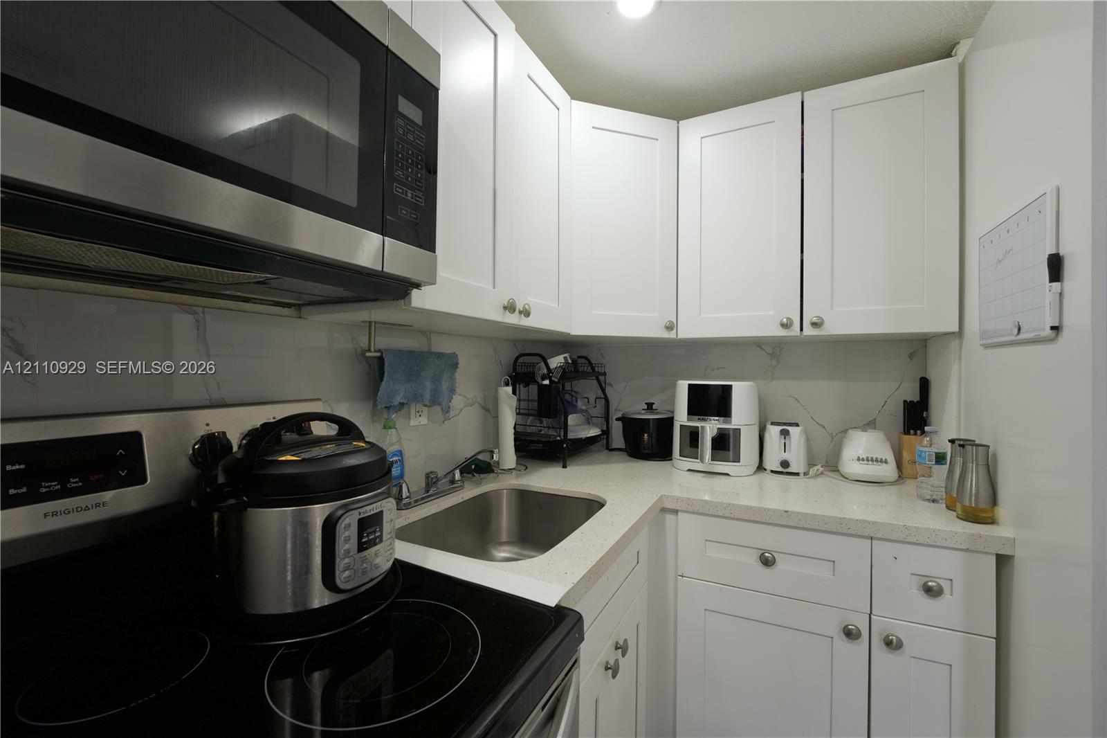 Kitchen featuring white shaker-style cabinetry, stainless steel microwave, stone-finish countertops, stainless steel undermount sink, and stone-finish backsplash