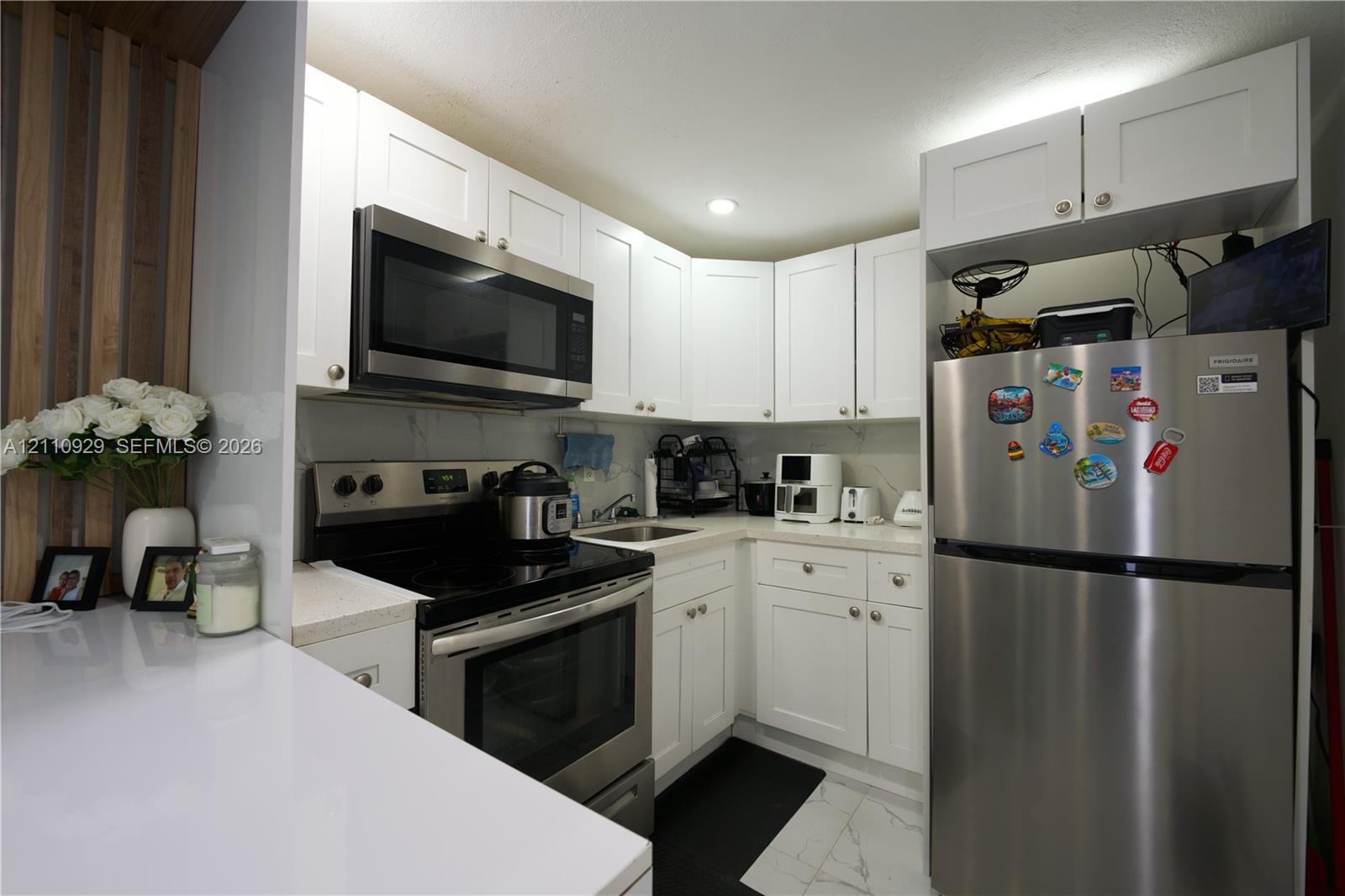 Kitchen featuring white Shaker-style cabinetry, stainless steel appliances, white stone-composite countertops, and a full-height stone-finish backsplash