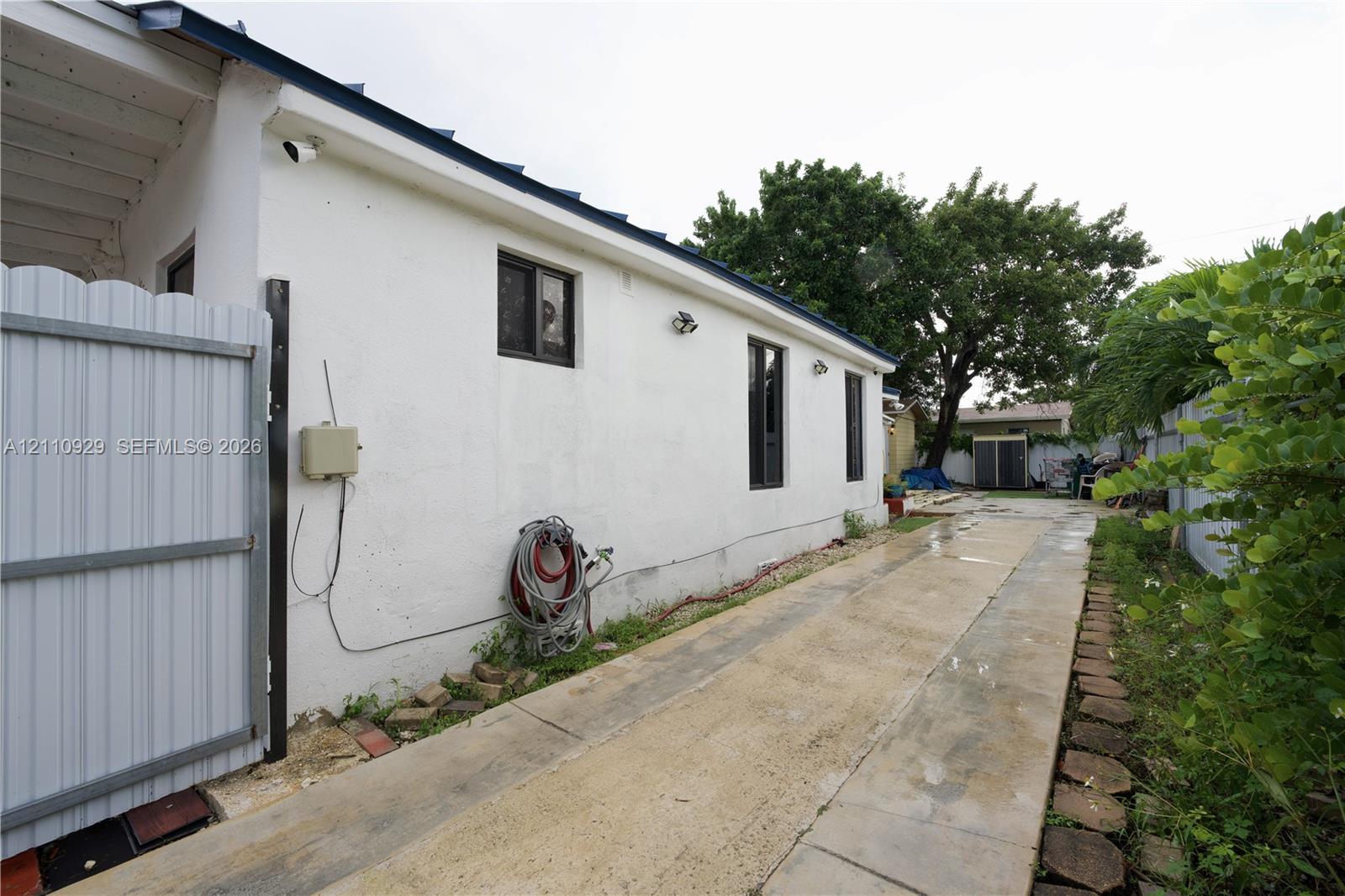 Stucco exterior finish with inset windows, white metal side gate, and concrete paved pathway