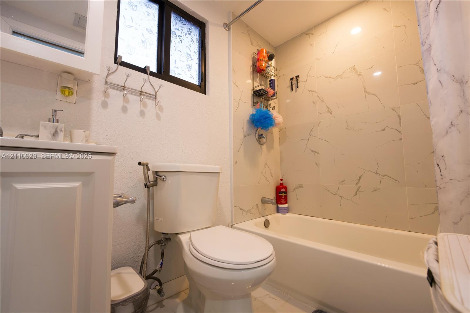 Full bathroom featuring a white vanity cabinet, a tub-shower combination with light-toned wall tile, a window, and chrome hardware