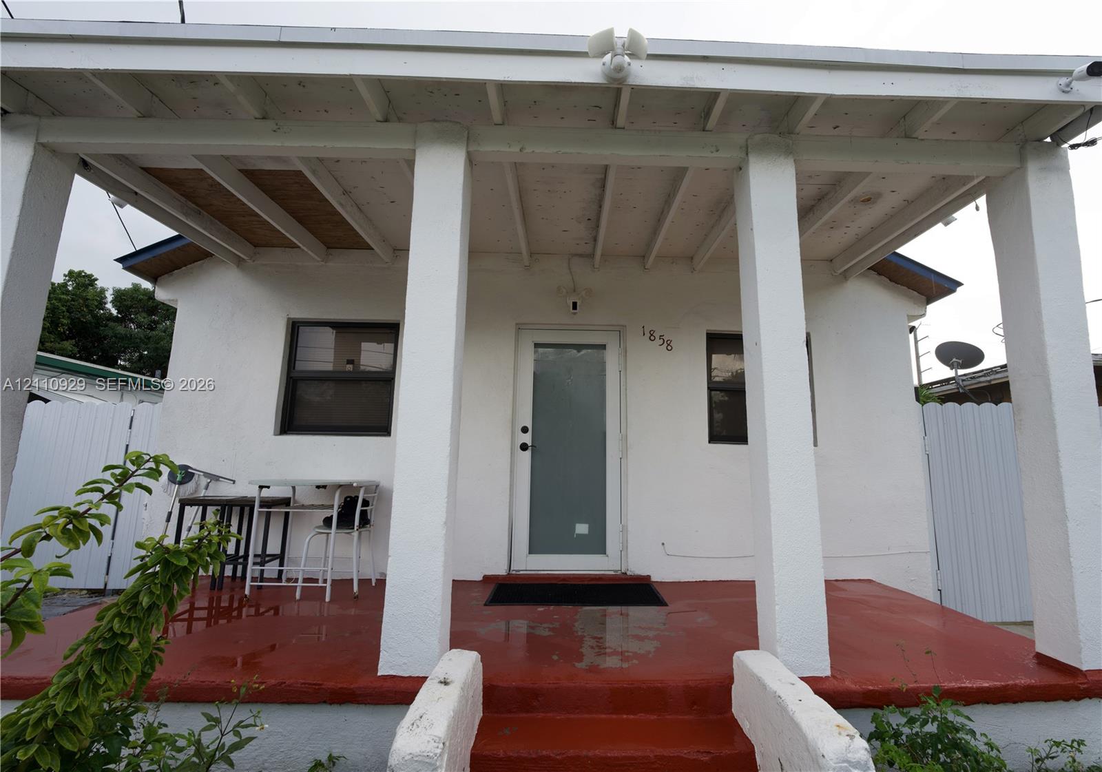 Covered front porch featuring structural columns, a painted concrete floor, exposed wood ceiling rafters, and an exterior door with a frosted glass panel Covered front porch featuring structural columns, a painted concrete floor, exposed wood ceiling rafters, and an exterior door with a frosted glass panel