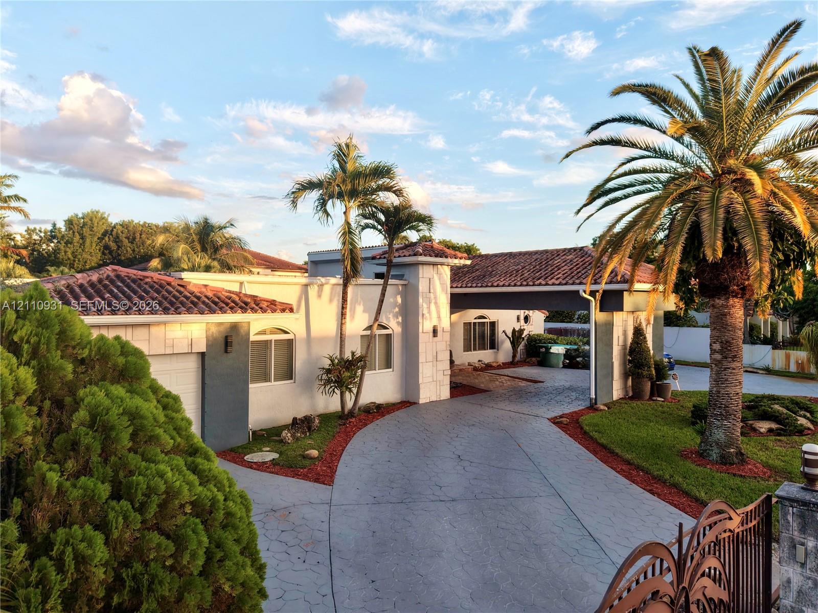 Single-story exterior featuring a clay tile roof, arched windows, covered carport, and paved circular driveway