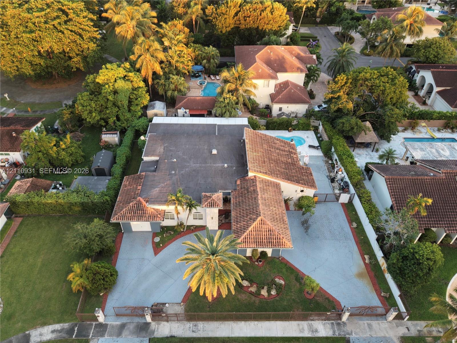 Single-story residence featuring a clay tile roof, expansive paved driveway, swimming pool, and mature perimeter landscaping