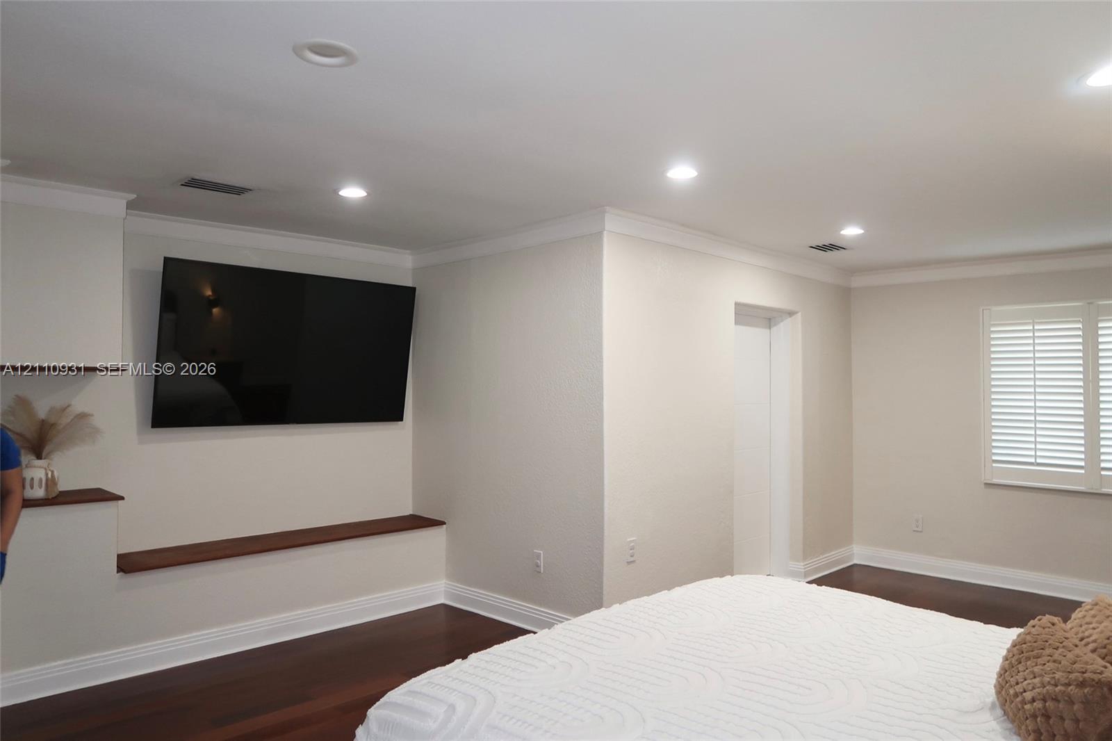 Dark wood-finish flooring, recessed lighting, crown molding, integrated wood-finish shelving, and plantation shutters