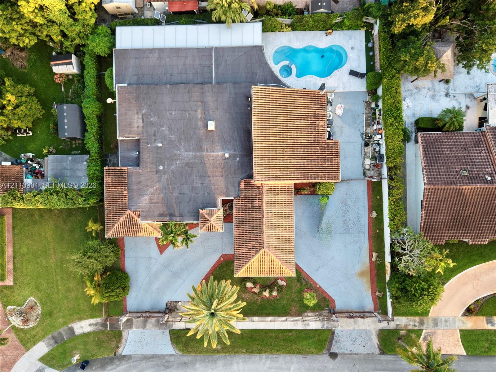 Aerial perspective featuring a tile roof, an in-ground swimming pool, a sprawling paved driveway, and mature landscaping