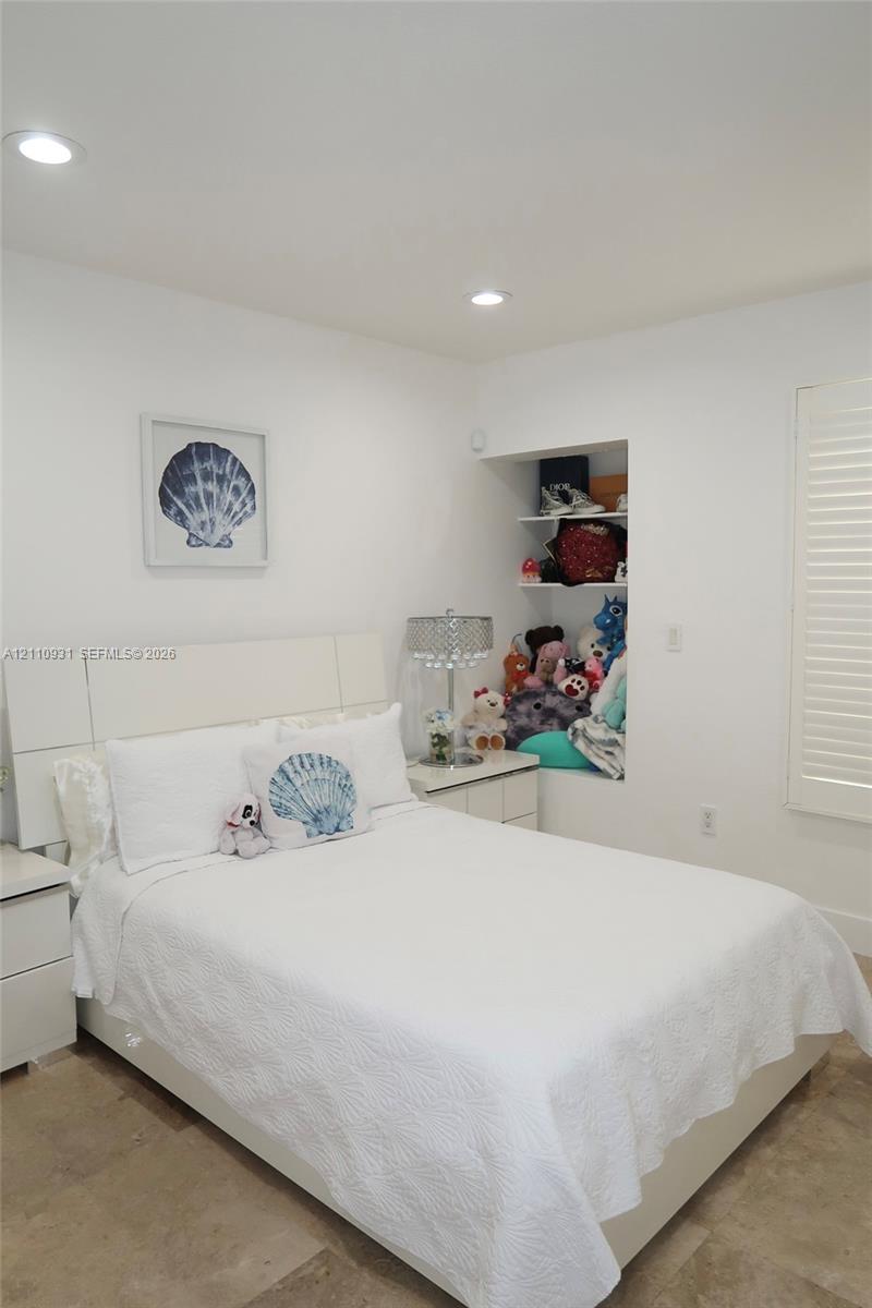 Neutral-toned tile flooring, built-in recessed shelving, integrated ceiling lighting, and plantation-style window shutters