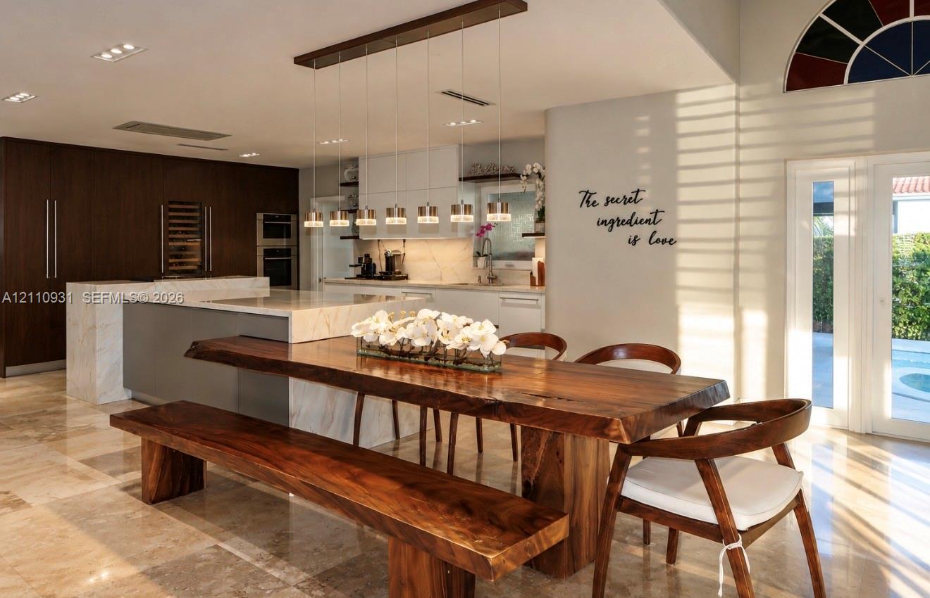 Kitchen featuring a stone-surface island, dark-toned cabinetry, recessed ceiling lighting, multi-pendant light fixture, and polished stone flooring