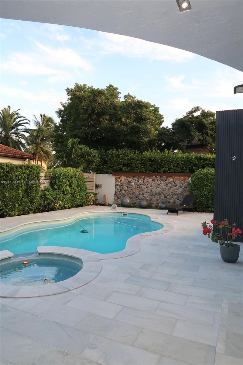 Free-form swimming pool with integrated spa, stone-accented perimeter wall, and light-toned paved decking