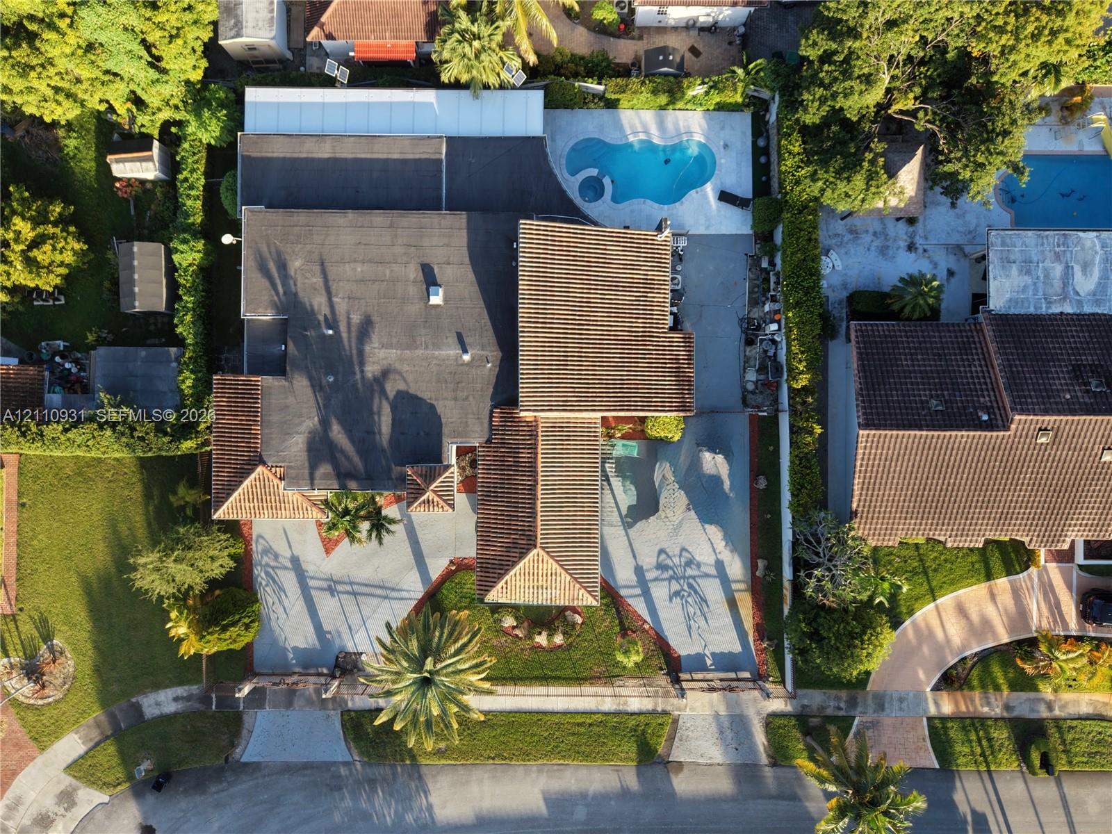 Aerial perspective of a multi-section roofline, expansive concrete driveway, and backyard pool area with integrated hardscaping