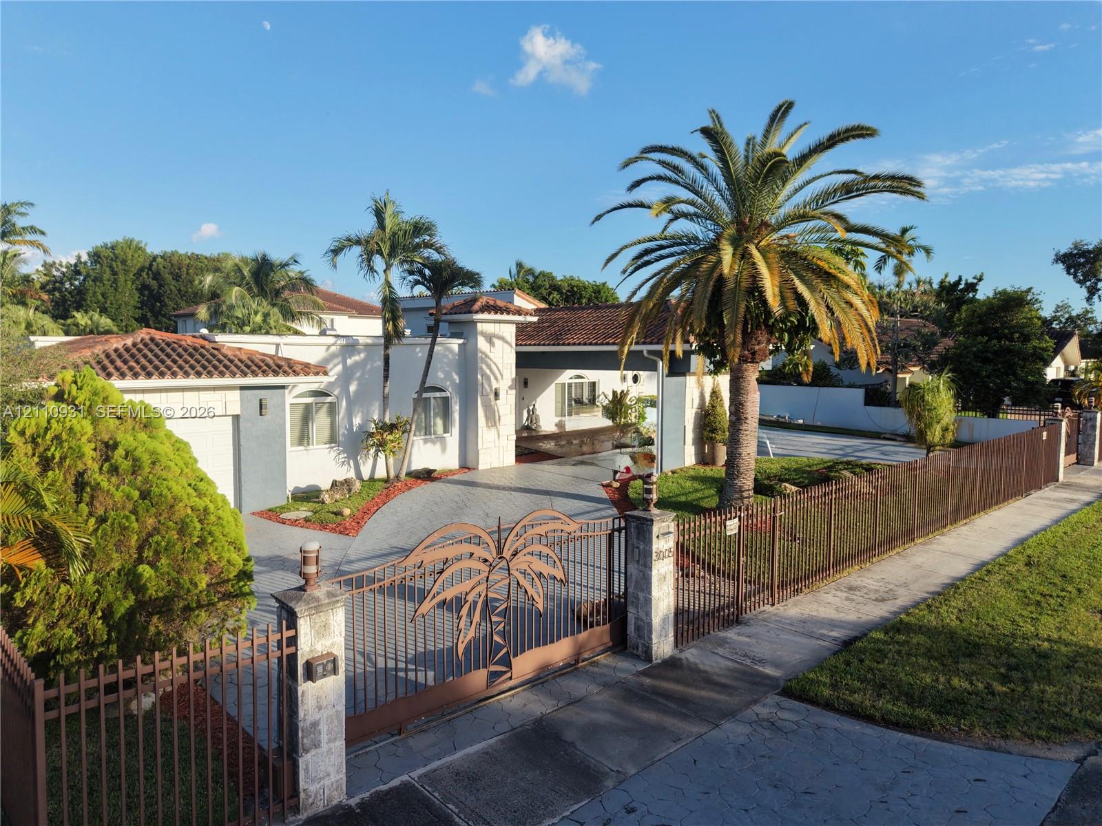Single-story residence featuring a tile roof, decorative metal security gate, paved driveway, masonry perimeter fencing, and mature landscaping