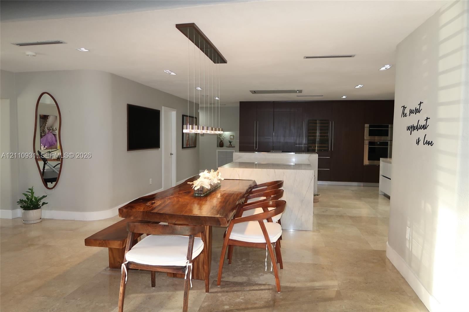 Open-concept kitchen featuring dark wood cabinetry, integrated double wall ovens, built-in wine refrigeration, and a large stone-surfaced kitchen island, complemented by stone tile flooring and recessed ceiling lighting