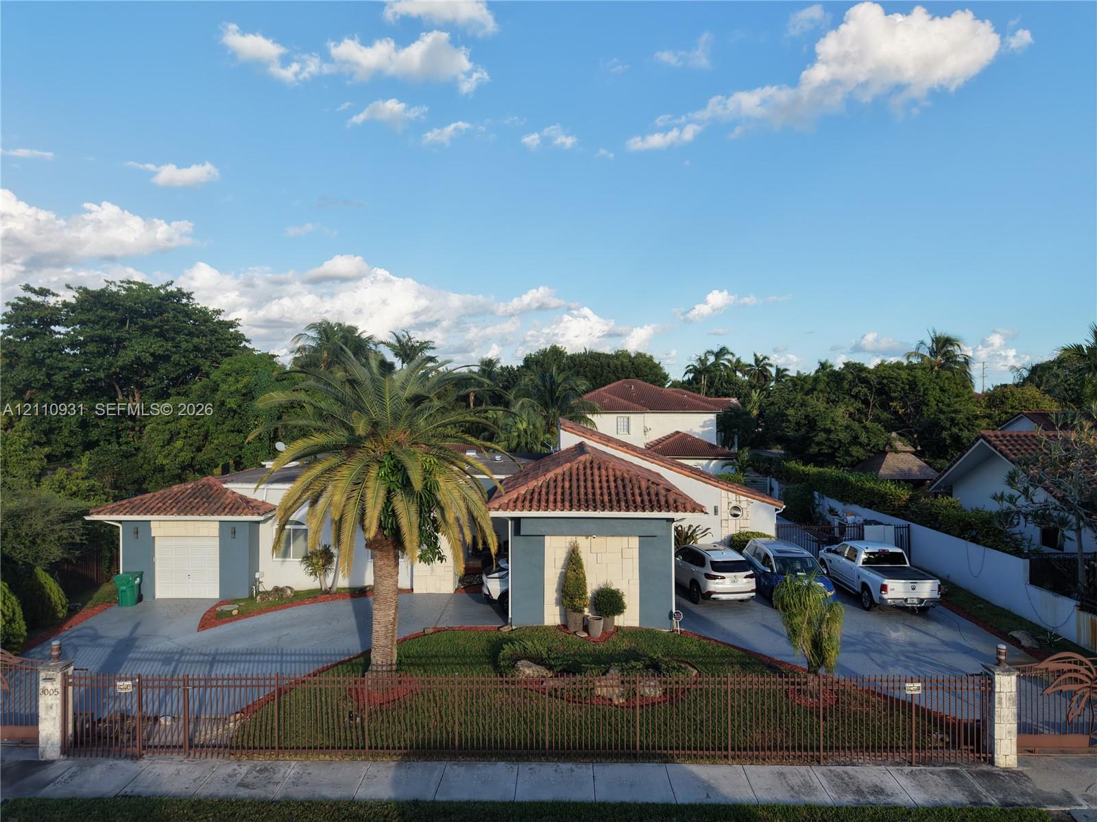 Single-story residence featuring a Mediterranean-inspired tile roof, masonry facade accents, an attached two-car garage, expansive concrete driveway, and a perimeter metal fence