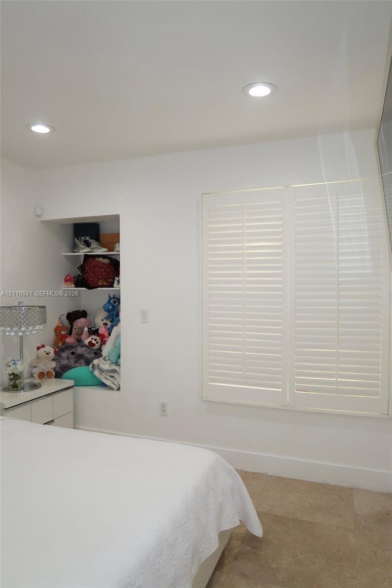 Built-in recessed shelving, plantation shutters, recessed lighting, and stone flooring