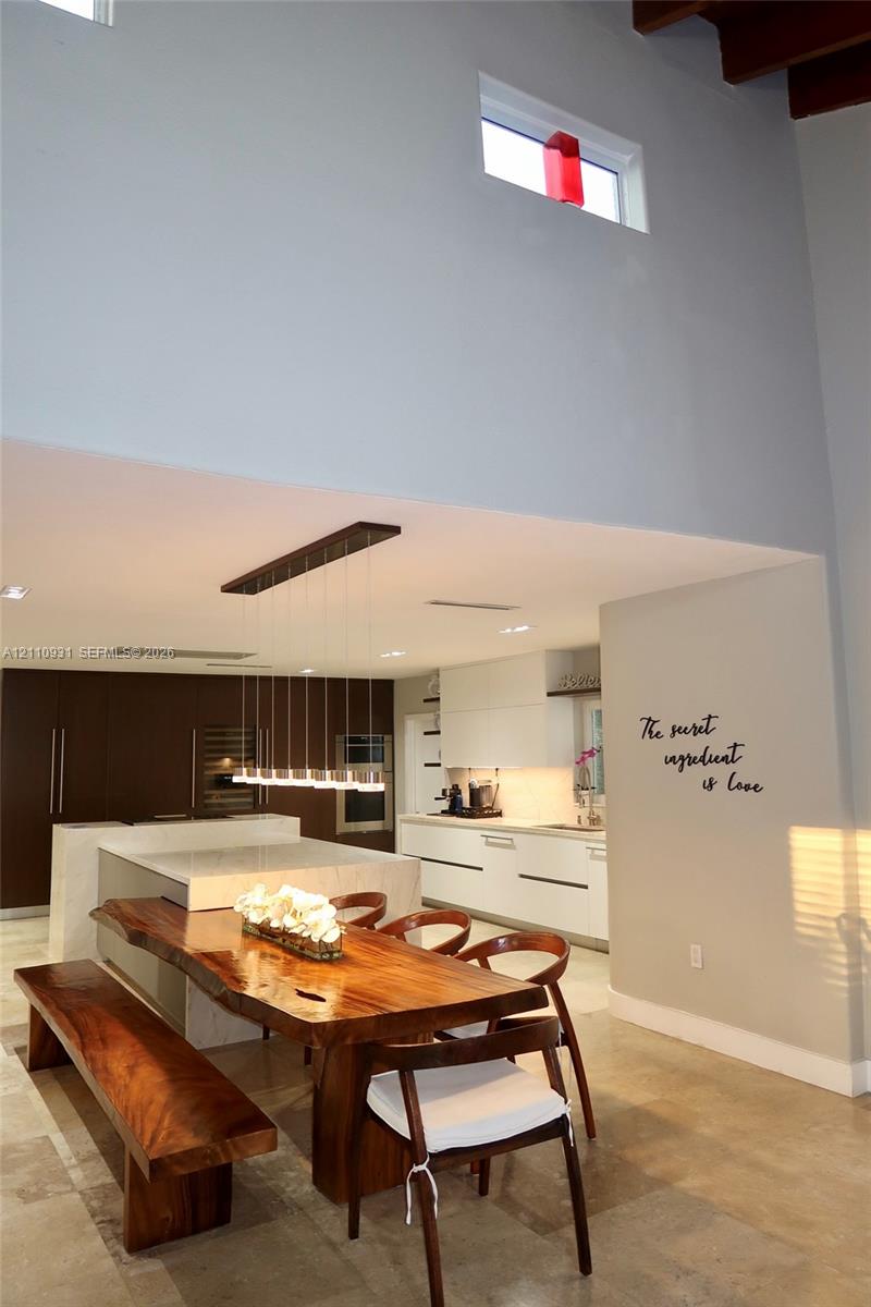 Modern kitchen featuring flat-panel cabinetry, a central island with a stone-surface waterfall edge, high ceilings with exposed wood beams, clerestory windows, and recessed lighting