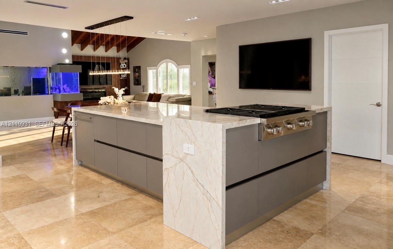 Kitchen island featuring a waterfall stone countertop, integrated gas cooktop, matte-finish cabinetry, and polished tile flooring