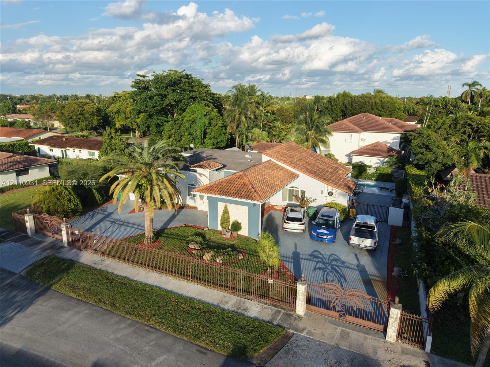 Single-story residence featuring a clay tile roof, expansive paved driveway, decorative metal perimeter fencing, and mature landscaping