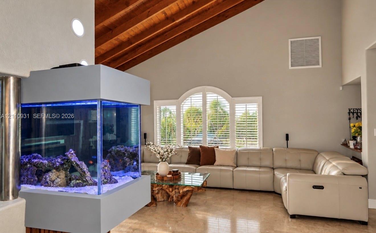 Vaulted ceilings featuring exposed wood beams, built-in structural aquarium, arched window with integrated plantation shutters, and polished stone flooring