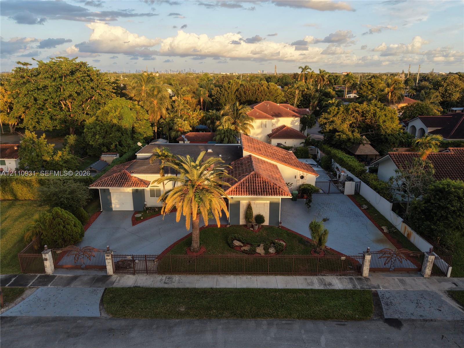Single-story residence featuring a terracotta-tiled roof, an expansive paved driveway, and decorative metal perimeter fencing