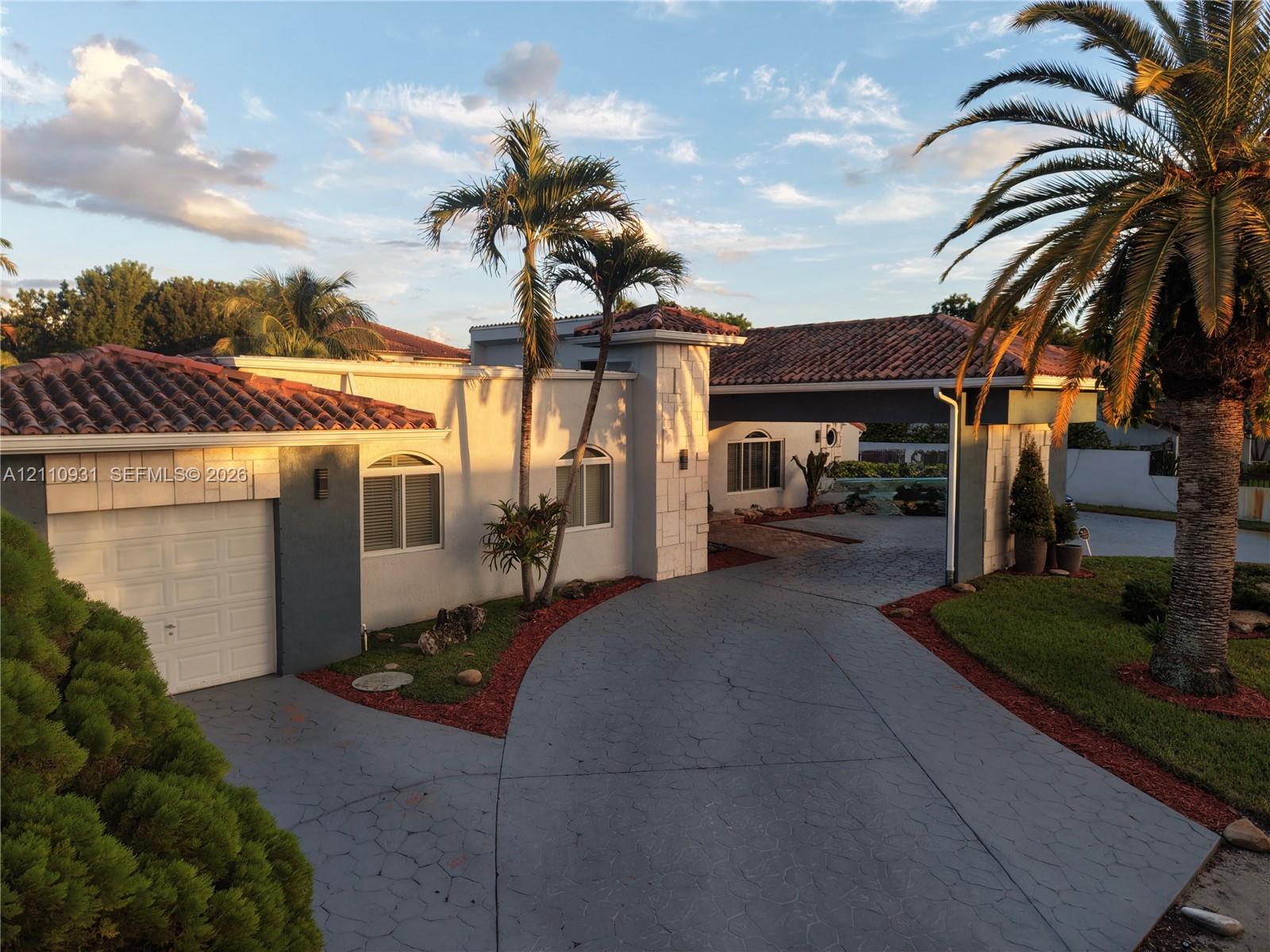 Stucco exterior featuring arched windows, a multi-car covered porte-cochre, decorative stone accents, and a tile roof