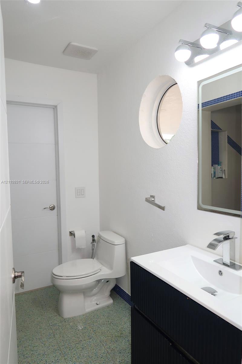 Bathroom featuring a black vanity with a white countertop and integrated sink, chrome-finish faucet, circular accent window, and wall-mounted vanity light fixture