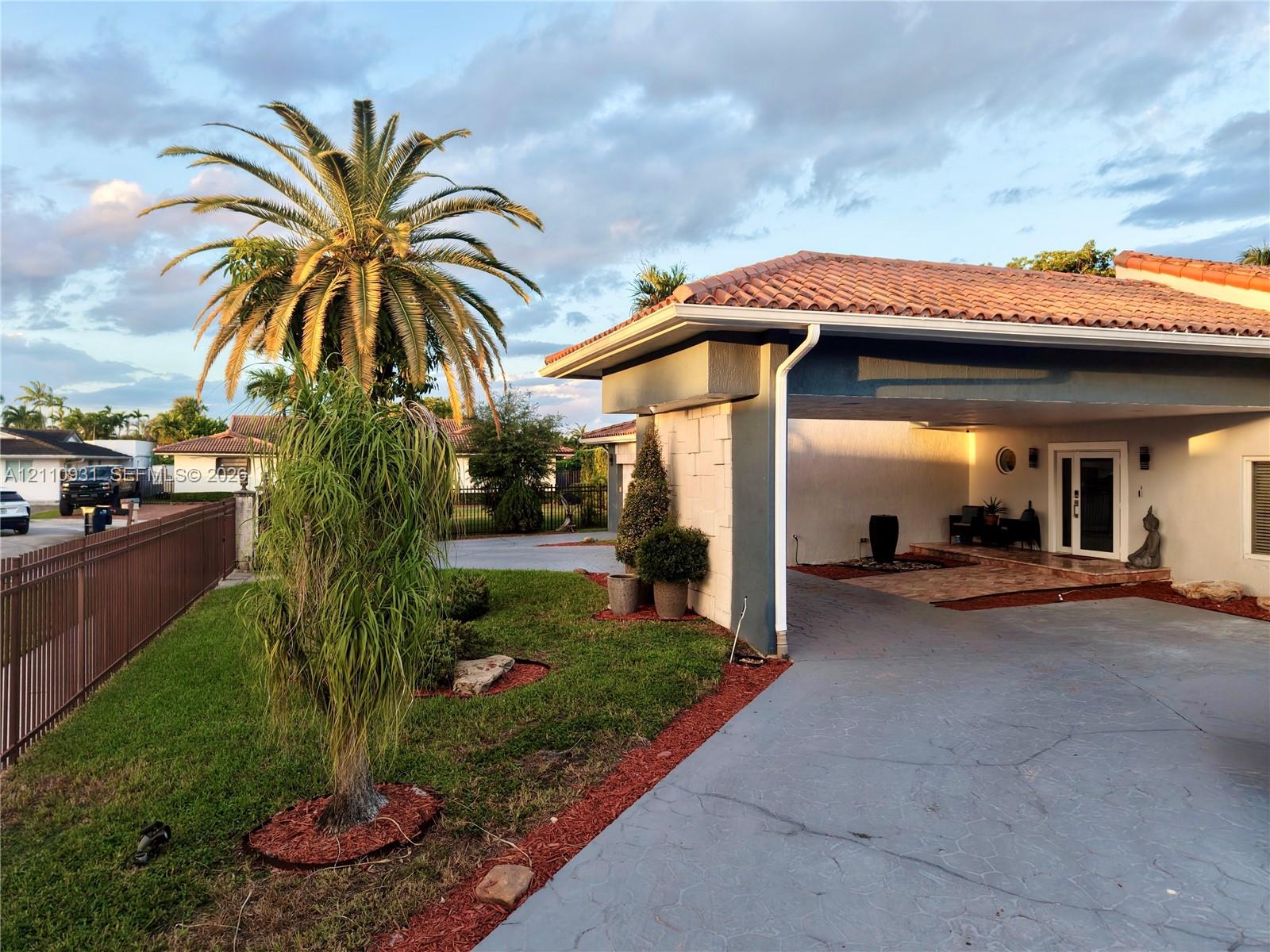 Exterior facade featuring a terracotta-tiled roof, covered entryway, textured masonry detailing, concrete driveway, and mature palm landscaping