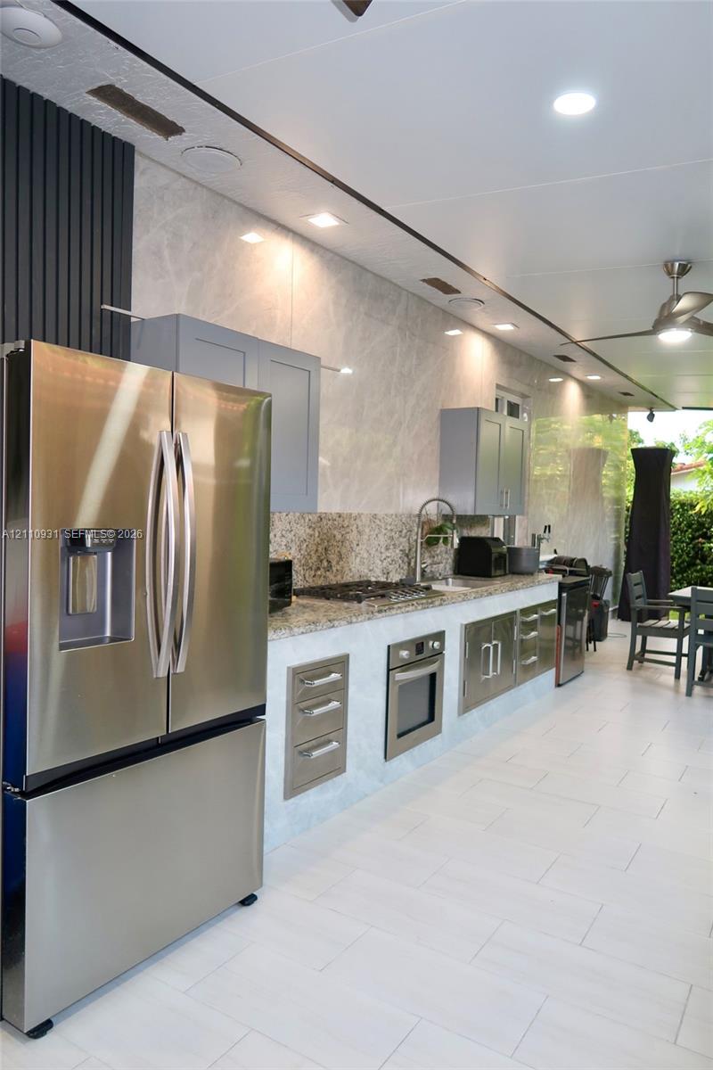Outdoor kitchen featuring stone countertops, stainless steel appliance suite, recessed lighting, tile flooring, and integrated cabinetry
